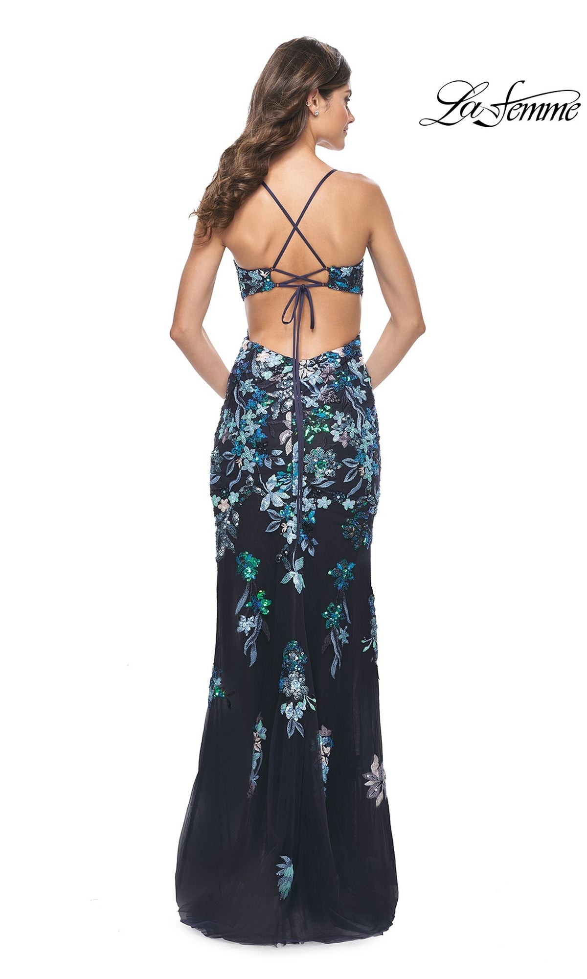 Woman wearing the La Femme Floral-Sequin Long Prom Dress 31992, a floor-length gown with floral embroidery, open back, and crisscross straps, standing against a white background.